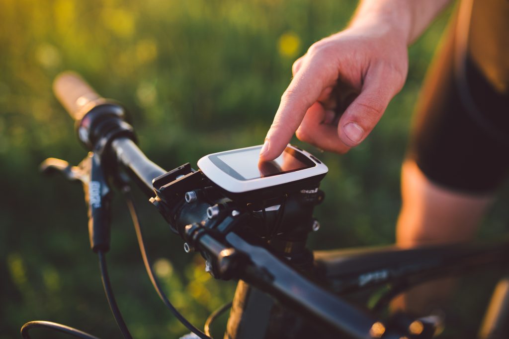 A young brunette guy on a mountain bike uses a cycling computer, a navigator in the field at sunset of the day