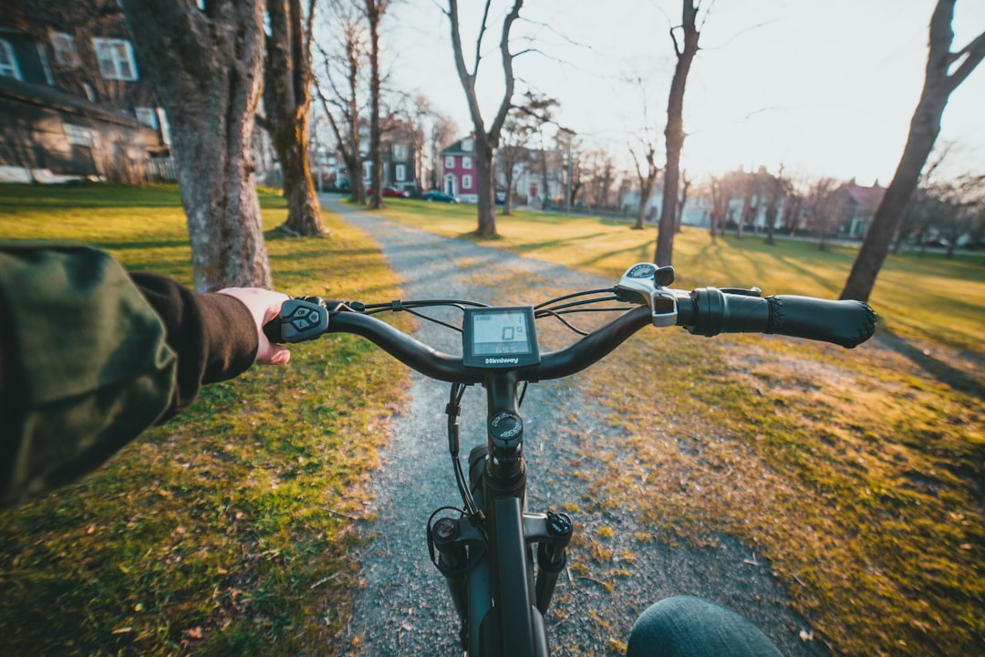 A close-up shot of a hand holding a smartphone displaying a map application, with a bicycle and an urban setting softly blurred in the background.