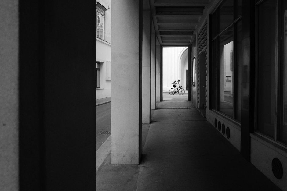 A person stands with their bicycle at the entrance of a scenic and quiet city alley, looking curious and ready to explore an unconventional route.